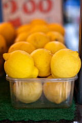 Bright yellow lemons packed in a transparent container at local market.