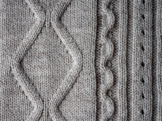 Neutral gray wool and cashmere knitwear with braid cable stitch knitted pattern, cozy winter textile background.