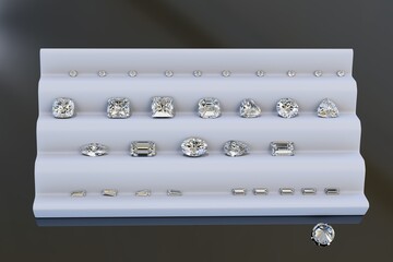 Variously cut diamonds: round brilliant, cushion, heart, asscher, radiant, emerald, baguette, oval, pear, marquise, trilliant, on white tray on dark background.