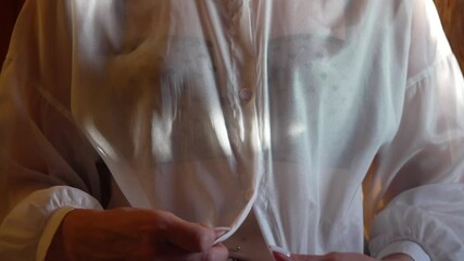 Hands Buttoning Shirt Woman fastening sheer white shirt getting dressed indoors