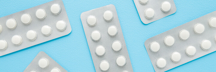 New blister packs of white pills on light blue table background. Pastel color. Wide banner. Closeup. Medicine pattern. Flat lay. Top down view.