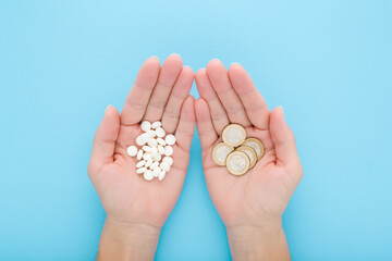 Young adult woman palms holding and showing heaps of white pills and euro coins on light blue table...