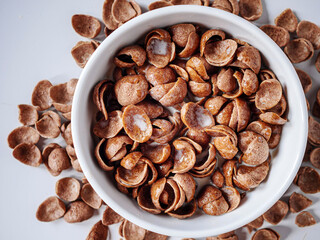 Chocolate corn flakes with milk in a bowl on white background, Top view