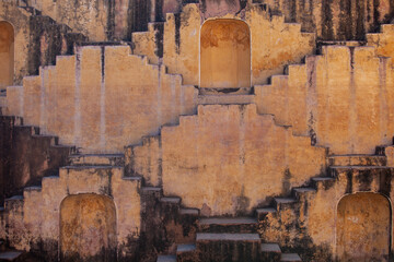 Intricate geometric patterns of a historic stepwell in India, featuring multiple flights of ancient, weathered stone stairs and arched alcoves, showcasing unique traditional architecture and water con