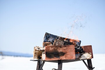 Firewood burning on a metal grill in a snowy winter landscape