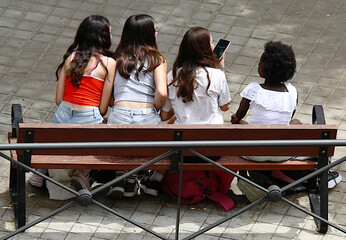 Niñas adolescentes de diferentes nacionalidades sentadas juntas con el móvil divirtiéndose en un...