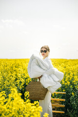 Woman carrying a blanket in a bright yellow flower field during a sunny day