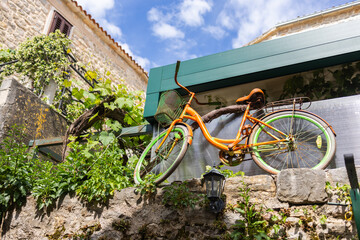 Vintage orange bicycle on stone wall with greenery. Creative outdoor decor, urban retro charm, and...