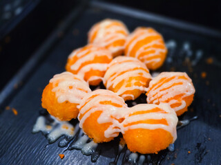 Sushi balls drizzled with creamy mayonnaise, arranged on a black tray. A close-up shot showcasing...