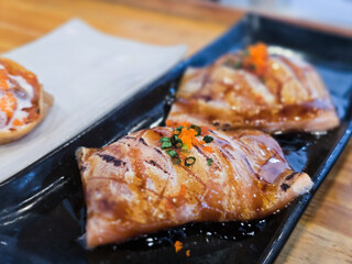 Grilled salmon sushi belly topped with fish roe and chopped scallions, glazed with teriyaki sauce and served on a black ceramic plate