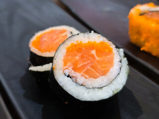 Maki sushi rolls filled with fresh salmon, rice, tobiko, and wrapped in nori seaweed, served on a black ceramic plate in a Japanese restaurant.