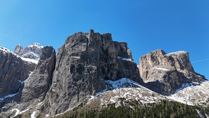 Steep mountain with snow on top and trees beneath. Photograph taken in the dolomites, italy in 4K with a drone. 