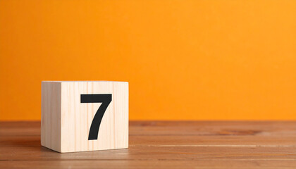 Wooden cube with number 7 on wooden table with orange wall on background.