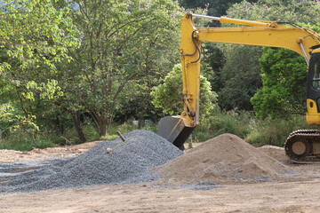 Yellow backhoe with piles of sand and rocks for mixing cement in a forest area for the construction...