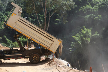 Obraz premium A white truck is dumping sand on the ground on a rural road through a forest being repaired, in the construction area of ​​a road repair contractor.