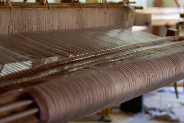 A close-up view of a traditional loom in action, showcasing intricate threads being woven into...