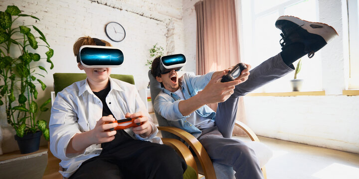 Father and son are immersed in a virtual reality gaming experience in a cozy living room setting. Concept of modern entertainment and digital interaction in family spaces.