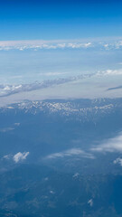 Aerial view from airplane window at high altitude of distant mountains covered with snow and puffy...