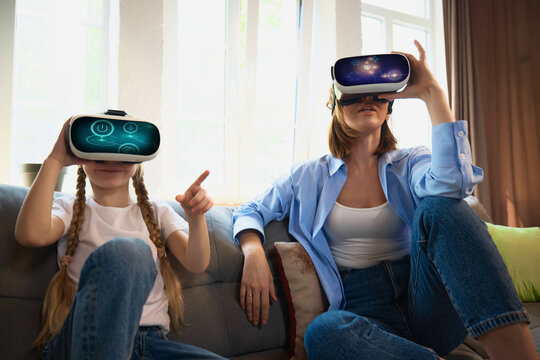 A mother and daughter enjoy a virtual reality experience in a cozy living room. Concept of family bonding through technology and shared digital experiences. - Powered by Adobe
