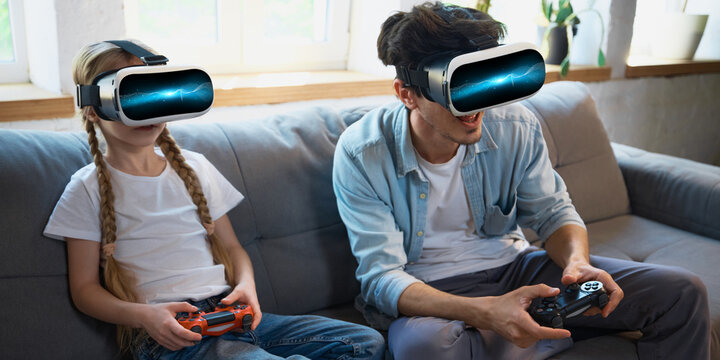 Father and daughter are enjoying a virtual reality gaming experience on their couch at home. Concept of family bonding through technology.