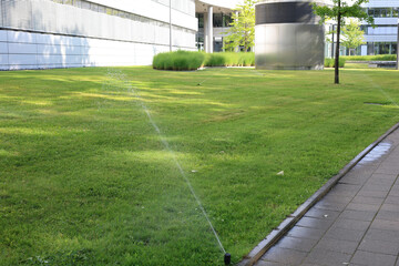 Sprinkler system watering a lush green lawn on a sunny day.