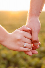 Loving couple holding hands showing engagement ring at sunset