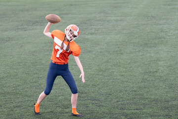 A youth football player, dressed in bright orange gear, prepares to throw a football on a...