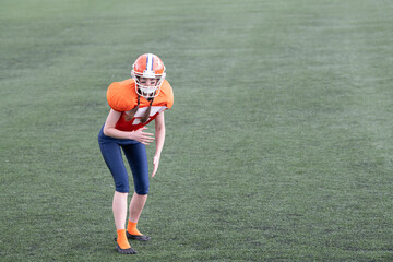 A young female athlete crouches on a grassy field, preparing for a play. She is dressed in an...