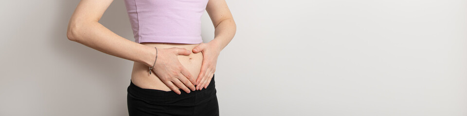 A young woman stands with her hands pressed against her abdomen, displaying signs of discomfort....