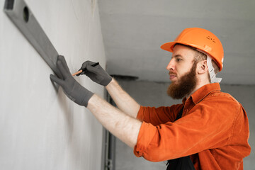 Portrait of a bearded builder using a spirit level to measure a wall.