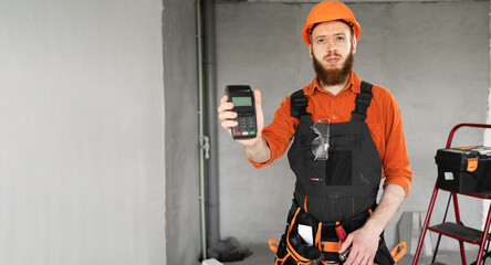 Smiling builder in hardhat holding a POS terminal for electronic payments