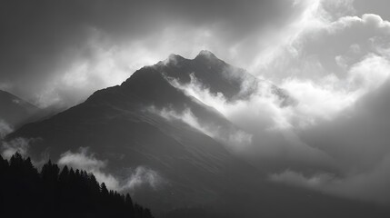 Fototapeta premium Dramatic black and white photograph of a massive mountain peak shrouded in turbulent low hanging clouds.