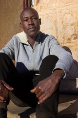 village single african man sited in front of the house in the yard, sunny day