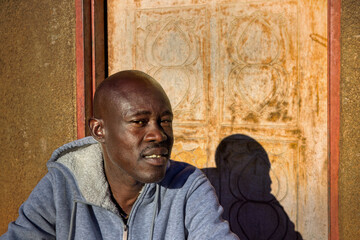 village single african man sited in front of the house in the yard, sunny day