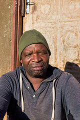 village single african man sited in front of the house in the yard, sunny day