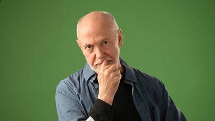 A senior man with a beard expresses joy while listening to happy secret, set against a vivid green screen backdrop. His attire is casual yet expressive.