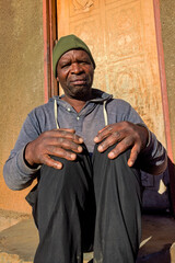 village single african man sited in front of the house in the yard, sunny day