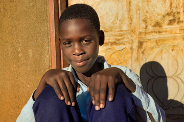 village single african school boy sited in front of the house wearing uniform