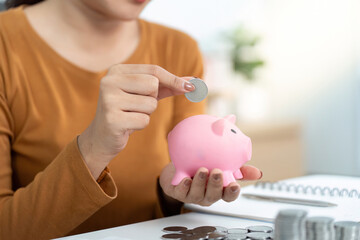 Savings and Financial Planning. Individual adding coins to pink piggy bank.