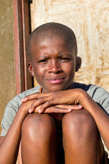 village single african boy sited in front of the house , in the yard, sunny day,