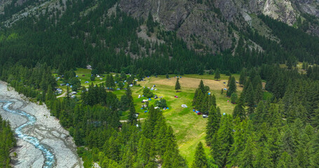 AERIAL: Forest clearing in a mountain valley filled with tents and RVs. Beautiful campsite,...