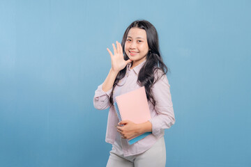 A woman is smiling and waving at the camera while holding a stack of books. Concept of happiness...