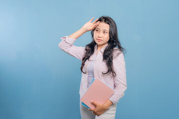 A woman is holding a blue book and a pink book. She is looking at the camera and she is thinking