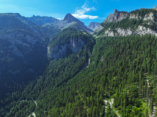 AERIAL: Towering, rugged mountain peaks above a vast, dense green forest that fills valley and...