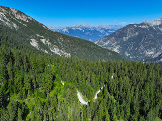 AERIAL: Road winds along a mountain ridge, covered in dense, vibrant green forest, with towering...