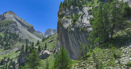 AERIAL: Picturesque climbing crag in remote alpine valley. Towering limestone cliff is streaked...