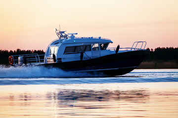 A river yacht, a speedboat, is sailing fast along the river at sunset. Evening rest on the water,...