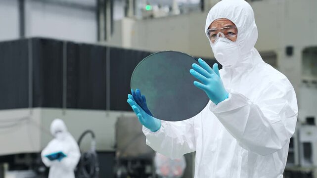 A male worker in a dustproof suit inspecting silicon wafers in a semiconductor factory