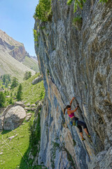 Female climber searches for grip while climbing an overhanging limestone wall. Fearless athlete is...