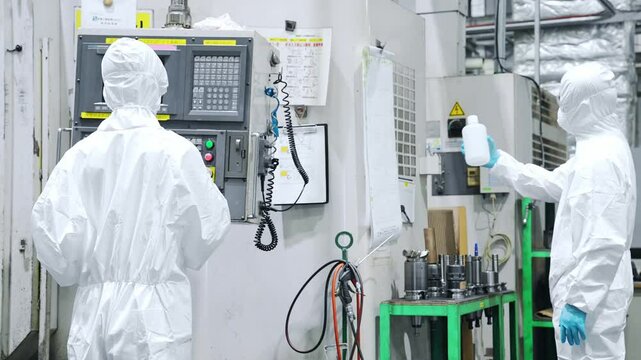 Rear view of male and female workers wearing protective clothing walking through a factory